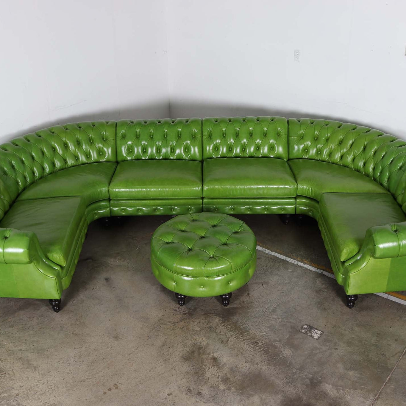 Green leather U-sectional sofa with matching ottoman on a concrete floor.